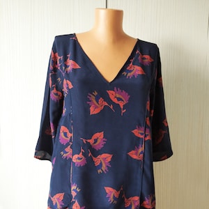 Può includere: Una blusa blu navy con stampa floreale con fiori arancioni, viola e marroni. La blusa ha un collo a V e maniche a tre quarti.
