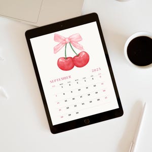 May include: A digital calendar for September 2025 with a watercolor illustration of two red cherries with a pink bow on top. The calendar is displayed on a tablet.