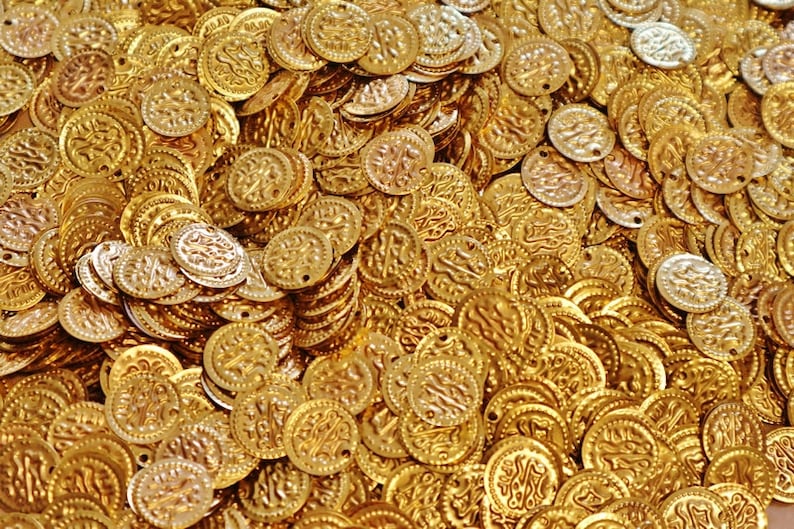 Pu&ograve; includere: Un grande mucchio di monete di metallo dorate con disegni intricati. Le monete sono disposte in modo casuale, creando una superficie testurizzata.