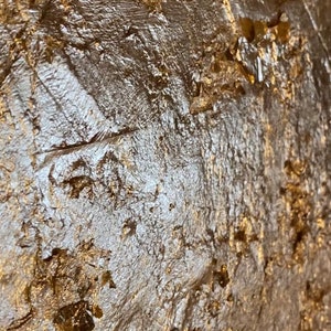 May include: Close-up of a textured gold surface with a metallic sheen. The surface has a rough, uneven texture with raised areas and crevices.