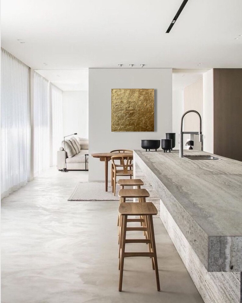 May include: A modern kitchen interior with a white countertop and a gold abstract painting on the wall. Four wooden bar stools are positioned in front of the countertop.
