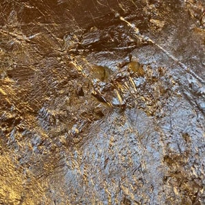 May include: Close-up of a textured, metallic surface with a gold finish. The surface has a wrinkled, crinkled appearance, creating a unique and abstract pattern.