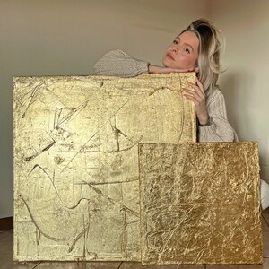 May include: Two gold leaf abstract paintings with textured surfaces. The larger painting has a more abstract design, while the smaller painting has a more geometric design.