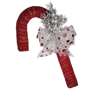 May include: A red and silver candy cane Christmas wreath with a white and red polka dot bow and silver sprigs.