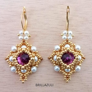 May include: A pair of gold earrings with a purple gemstone center and white pearl accents. The earrings are made with small gold beads and have a geometric design.