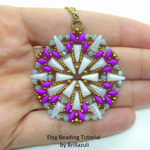 以下が含まれることがあります： 白、紫、金色の幾何学模様が施された丸いビーズのペンダントネックレス。ペンダントは、中心に星形の模様があり、その周りを同心円状のビーズが囲んでいます。