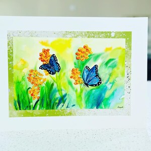 May include: A watercolor painting of a card with two blue butterflies on a green background with yellow flowers. The butterflies have black markings on their wings.
