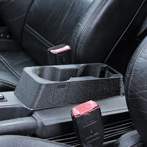 May include: Black leather car seat with a black plastic cup holder and a black seatbelt with a red buckle.