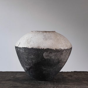 Peut inclure: Un vase en céramique blanc et noir de forme arrondie. La moitié supérieure du vase est blanche avec un glaçage craquelé, et la moitié inférieure est noire avec un glaçage moucheté.