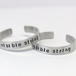 Peut inclure: Deux bracelets en argent gravés des mots "invisible string" et "visible string".