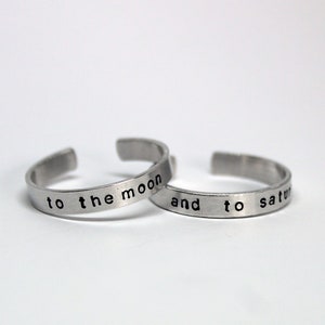 Puede incluir: Dos anillos de plata con el texto "to the moon and to saturn" grabado en ellos.
