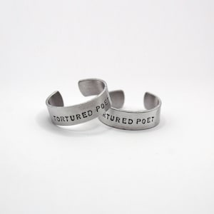May include: Two silver rings with the words "Tortured Poet" engraved on them.