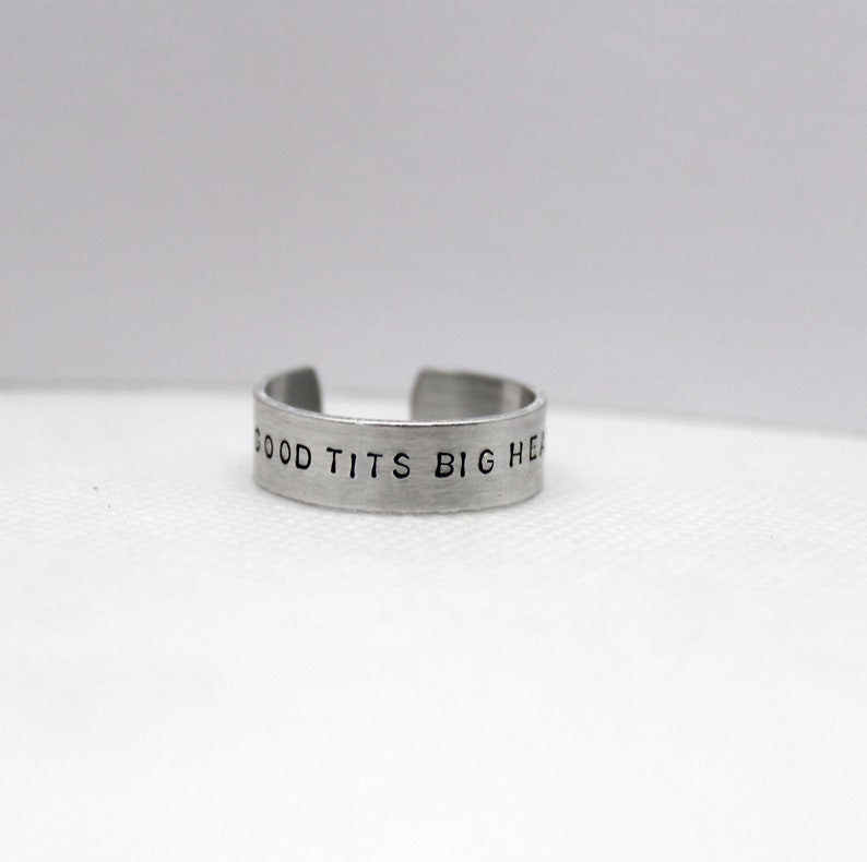 Puede incluir: Un anillo de plata con el texto "GOOD TITS BIG HEART" grabado en &eacute;l.