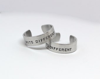 May include: Two silver rings with the phrase "Hits Different" engraved on them.