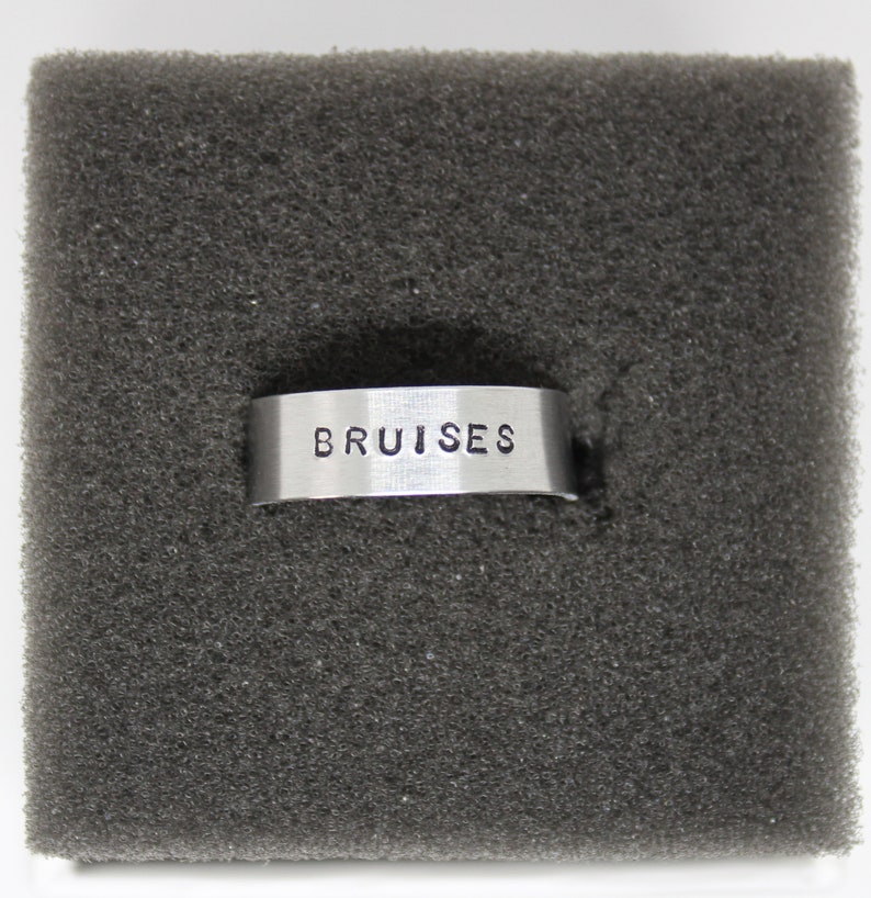 Puede incluir: Un anillo de plata con la palabra "BRUISES" grabada.