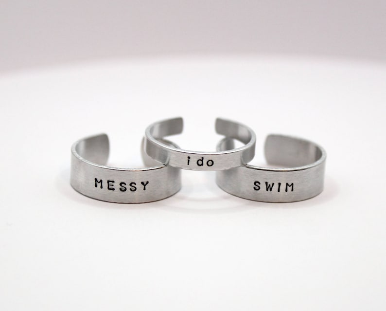 Puede incluir: Tres anillos de plata con las palabras "messy", "i do" y "swim" grabadas.