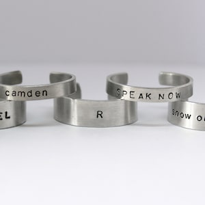 Peut inclure: Quatre bracelets en métal argenté avec des inscriptions gravées différentes. Les bracelets portent les inscriptions "Snow Angel", "camden", "Speak Now" et "snow on the beach".