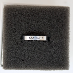 Puede incluir: Un anillo de plata con las palabras "too well" grabadas.