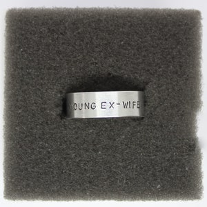 Puede incluir: Un anillo de plata con las palabras "YOUNG EX-WIFE" grabadas.