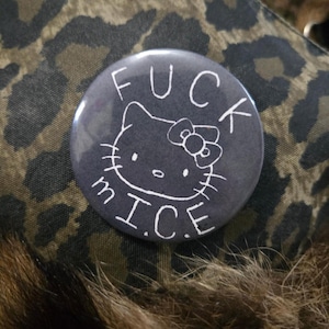 May include: A circular pin-back button with a dark gray background. The center features a white line-art illustration of a cat face with a bow on its ear. The text FUCK MICE is printed in white capital letters above and below the cat illustration.