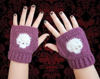 May include: A pair of fingerless gloves crocheted from dark purple yarn, each featuring a white skull motif centered on the back of the hand. The gloves have a ribbed cuff design at the wrist and leave the fingers exposed for full dexterity.