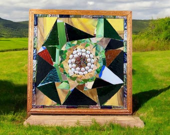 Könnte beinhalten: Ein gerahmtes Mosaik-Kunstwerk mit einem geometrischen Design, in dessen Mitte ein Kreis aus weißen Perlen von grünen, braunen und blauen Glasstücken umgeben ist.