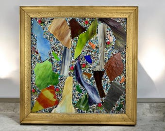 Könnte beinhalten: Ein gerahmtes Mosaik-Kunstwerk mit einer Vielzahl von bunten Glasstücken, die in einem abstrakten Muster angeordnet sind. Das Mosaik ist vor einem Hintergrund aus kleinen, schillernden Glasperlen platziert.