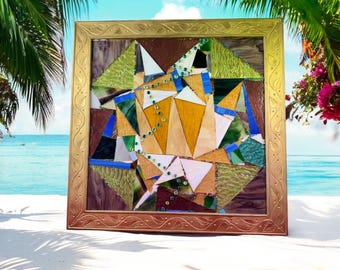 Könnte beinhalten: Ein gerahmtes Mosaikkunstwerk mit einem geometrischen Design, das verschiedene Farbtöne von grünem, blauem, braunem und gelbem Glas enthält. Der Rahmen ist golden mit einem Blattmotiv.