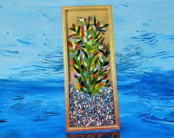 Könnte beinhalten: Ein gerahmtes Mosaik-Kunstwerk, das einen farbenfrohen Baum mit kleinen Vögeln zeigt, die auf den Ästen sitzen. Der Baum besteht aus kleinen Glassplittern in verschiedenen Grüntönen, Blau, Rot, Gelb und Orange. Der Hintergrund ist hellbraun und der Rahmen ist golden.
