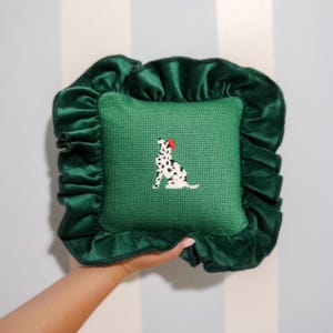 May include: A green velvet pillow with a ruffled edge features a white and black dalmatian dog with a red hat embroidered on the front.