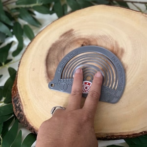 Puede incluir: Herramienta de plástico gris con un dial circular marcado con números y las palabras "Dilation (CM)" y "Engagement (%)." La herramienta se utiliza para medir la dilatación y el compromiso durante el trabajo de parto.