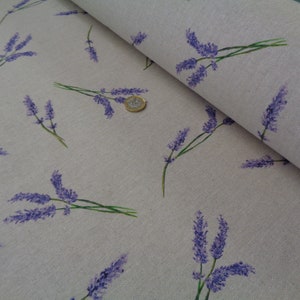 May include: A light beige fabric featuring a repeating pattern of lavender sprigs in purple and green. The fabric is folded, revealing its texture and design. A coin is visible on the fabric.
