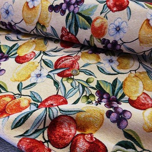 May include: Cream-coloured fabric featuring a pattern of lemons, grapes, and pomegranates. The design incorporates blue flowers and green leaves, creating a colourful textile. The fabric is rolled, displaying the pattern's repeat.