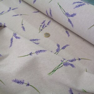 May include: A close-up of fabric featuring a lavender sprig pattern. The lavender is purple with green stems, set against a light beige backdrop. The fabric is folded, revealing its texture. Ideal for crafting or home decor projects.