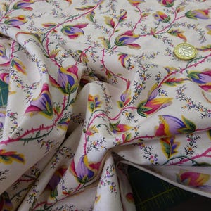 May include: White fabric with a floral print featuring pink, purple, yellow, and green flowers. The fabric is folded and has a coin on top.