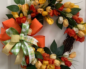 May include: A spring wreath with a green, orange, and yellow floral design. The wreath is decorated with a large orange bow with a green and yellow checkered ribbon.