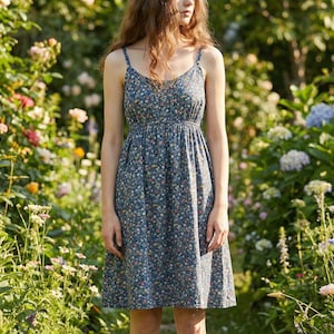 May include: A blue floral print dress with spaghetti straps. The dress has a fitted bodice and a flowing skirt. The dress is made of a lightweight fabric and is perfect for a summer day. The dress is surrounded by a garden of flowers.