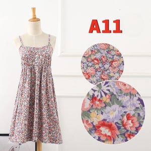 May include: A floral print sundress on a mannequin. The dress features a scoop neckline, spaghetti straps, and a gathered waist. The fabric is covered in small pink, red, and blue flowers. The text "A11" is in red in the upper right corner.