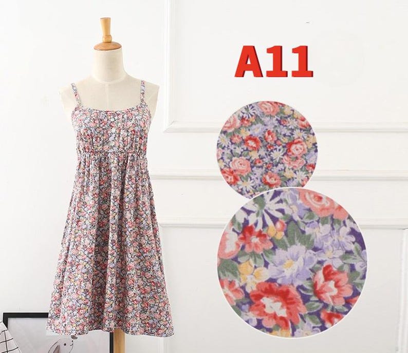 May include: A floral print sundress on a mannequin. The dress features a scoop neckline, spaghetti straps, and a gathered waist. The fabric is covered in small pink, red, and blue flowers. The text "A11" is in red in the upper right corner.