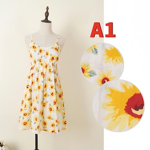 May include: A white sundress with a yellow sunflower pattern, displayed on a mannequin. The dress has thin straps and a gathered waist. Two circular images of sunflowers are next to the dress, and the text "A1" is above them.