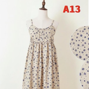 May include: A beige sundress with blue floral patterns is displayed on a mannequin. The dress features thin straps, a button-down bodice, and an elastic waist. The text "A13" is visible in the upper right corner.