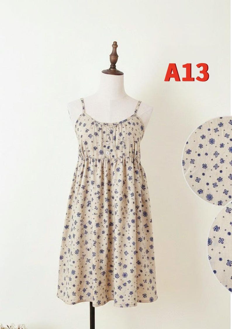 May include: A beige sundress with blue floral patterns is displayed on a mannequin. The dress features thin straps, a button-down bodice, and an elastic waist. The text "A13" is visible in the upper right corner.