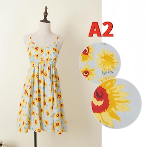 May include: Light blue sundress with a yellow sunflower print. The dress features spaghetti straps, a button-down bodice, and a gathered waist. The dress is displayed on a mannequin. The text "A2" is in the upper right corner.