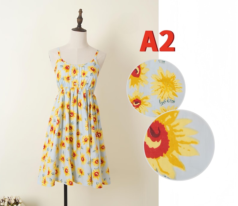 May include: Light blue sundress with a yellow sunflower print. The dress features spaghetti straps, a button-down bodice, and a gathered waist. The dress is displayed on a mannequin. The text "A2" is in the upper right corner.