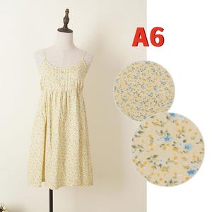May include: A light yellow sundress with a floral pattern of small blue and yellow flowers. The dress has thin straps and a pleated bodice. The text "A6" is in red in the upper right corner. Two circular fabric swatches show the floral pattern.