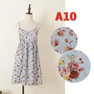 May include: A light blue sundress with a floral pattern, displayed on a mannequin. The dress features thin straps and a gathered waist. The floral print includes red, pink, and yellow flowers.