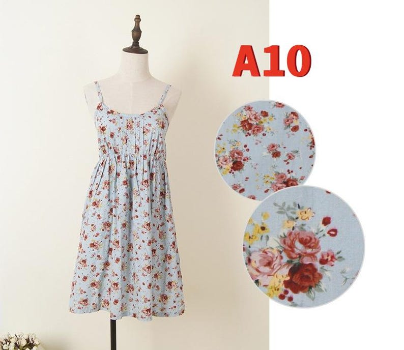 May include: A light blue sundress with a floral pattern, displayed on a mannequin. The dress features thin straps and a gathered waist. The floral print includes red, pink, and yellow flowers.