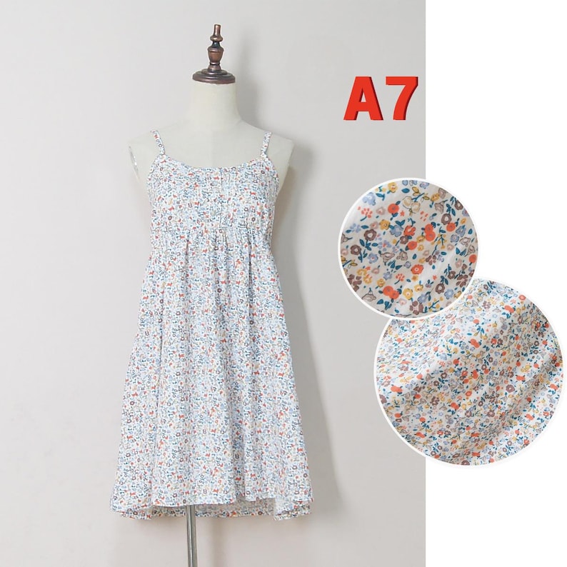 May include: A white sundress with a floral pattern, displayed on a mannequin. The dress features thin straps, a gathered bodice, and a knee-length skirt. The floral print includes small blue, orange, and yellow flowers on a white background. The dress is lightweight and appears suitable for warm weather.