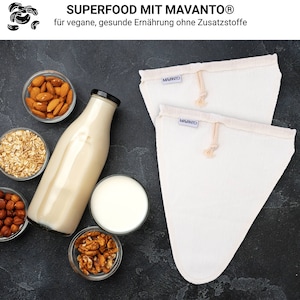 Könnte beinhalten: Zwei weiße Baumwoll-Nussmilchbeutel mit dem Aufdruck "MAVANTO". Die Beutel liegen auf einer dunkelgrauen Oberfläche mit einer Glasflasche Nussmilch, einer Schüssel Mandeln, einer Schüssel Haferflocken, einer Schüssel Haselnüssen und einer Schüssel Walnüssen.
