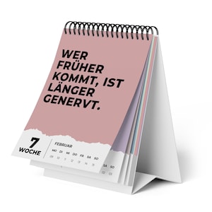 Op de afbeelding: Een bureaukalender met spiraalbinding, met een roze omslag met zwarte tekst die luidt: "WER FRÜHER KOMMT, IST LÄNGER GENERVT." De kalender toont de maand februari en de 7e week. De kalender staat op een witte standaard.